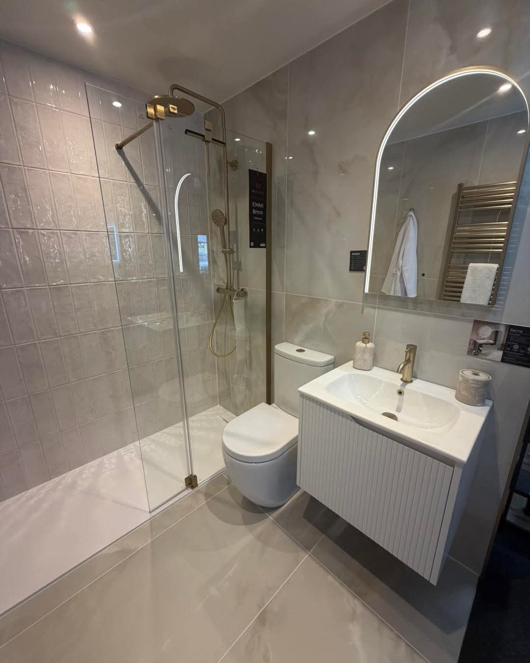 Finished bathroom with backlit arched mirror and gold-fitted shower