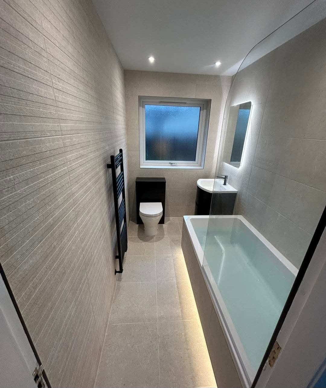 Wide view of a sculpted white tile statement bathroom with filled freestanding bath, a completed installation in Fife