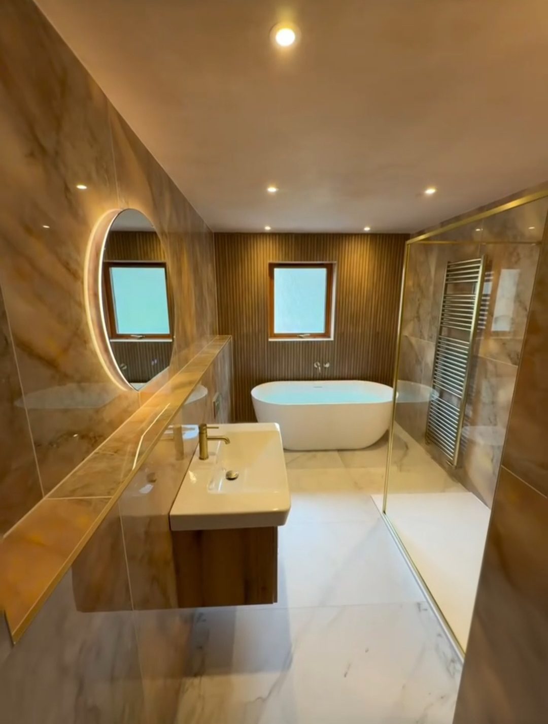 Luxury bathroom suite with gold fixtures and marble-effect tiling by BDR Bathroom Innovation