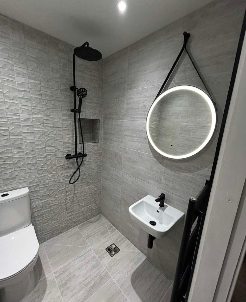 Tiled wet room installation in Fife with walk-in shower area, black fittings and round backlit mirror by BDR Bathroom Innovation