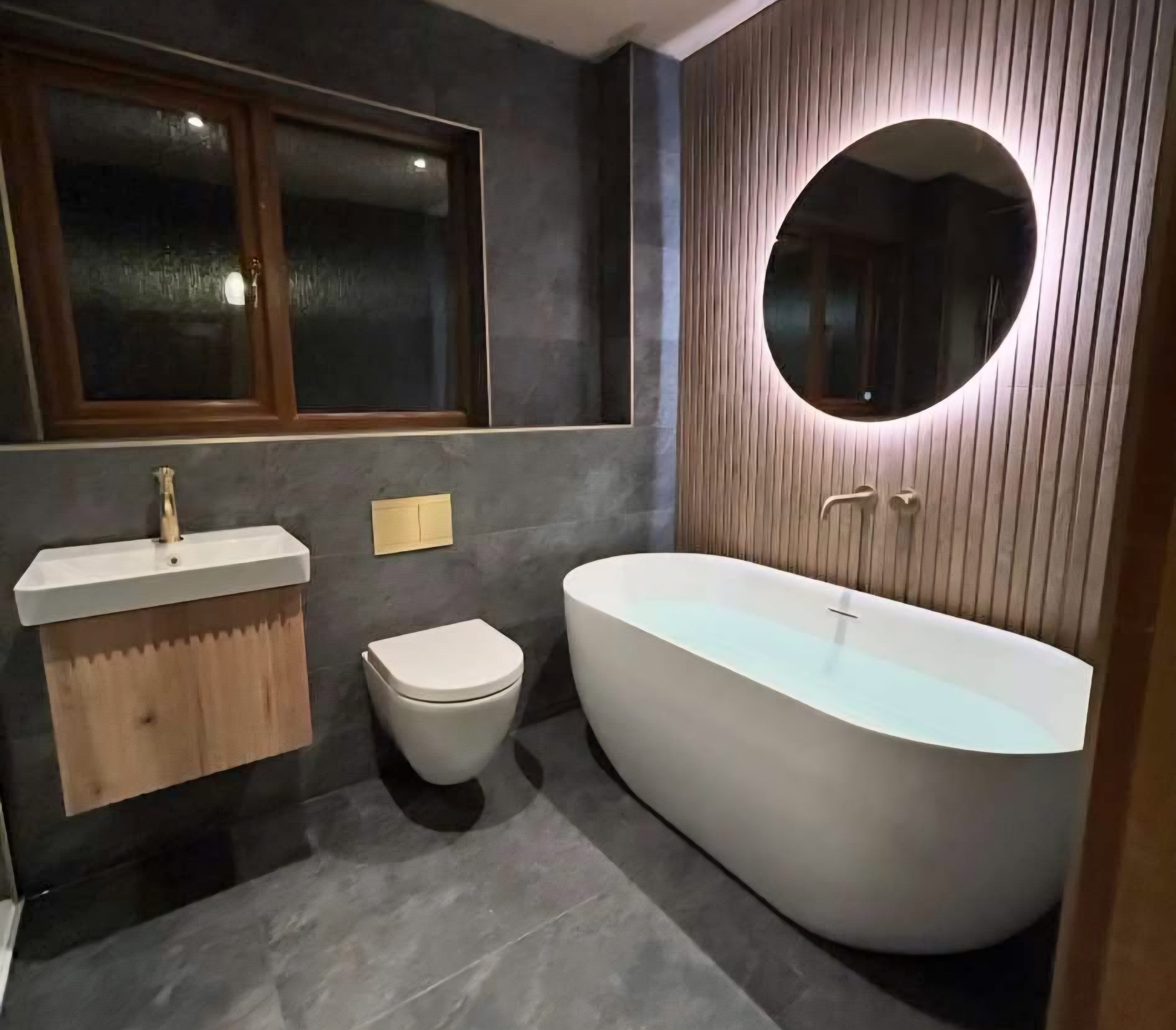 Freestanding bath with backlit round mirror and slatted wood feature wall fitted by bathroom fitters in Kirkcaldy