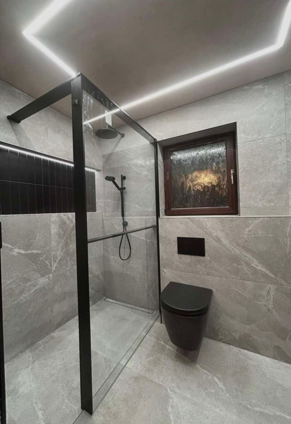 Walk-in wet room with black frame glass panel, dark wall-hung WC, and illuminated ceiling detail